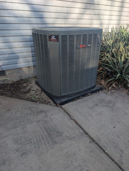 Residential outdoor air conditioning condenser beside a walkway